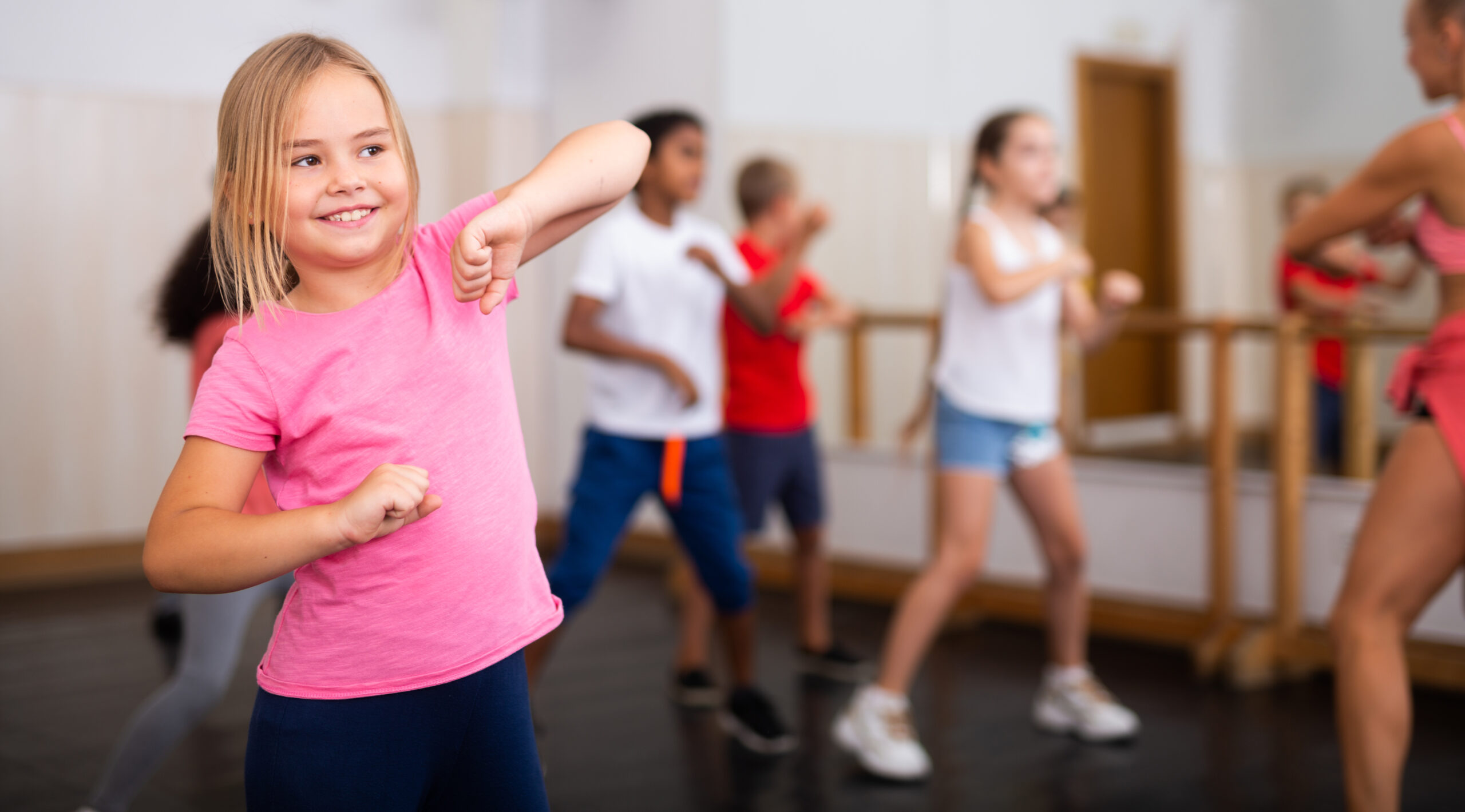 Preteen girl practicing dance movements with group of children Portrait of cheerful preteen girl practicing dance movements with group of children in choreography class